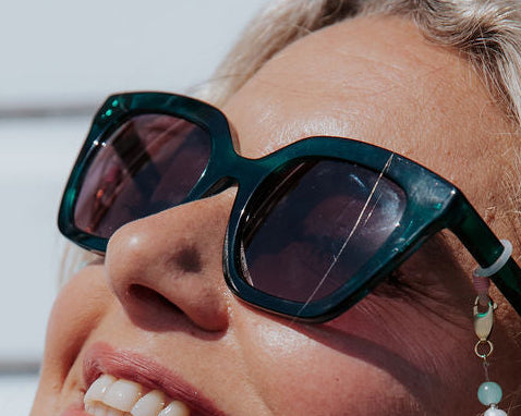 Woman wearing deep dark green high quality sunglasses looking up at the sun.